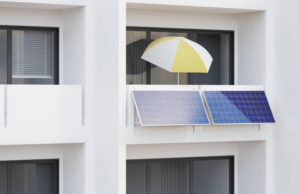 Balkon eines modernen Mehrfamilienhauses mit zwei montierten Solarpanels und gelb-weißem Sonnenschirm als Symbolbild für ein Balkonkraftwerk.