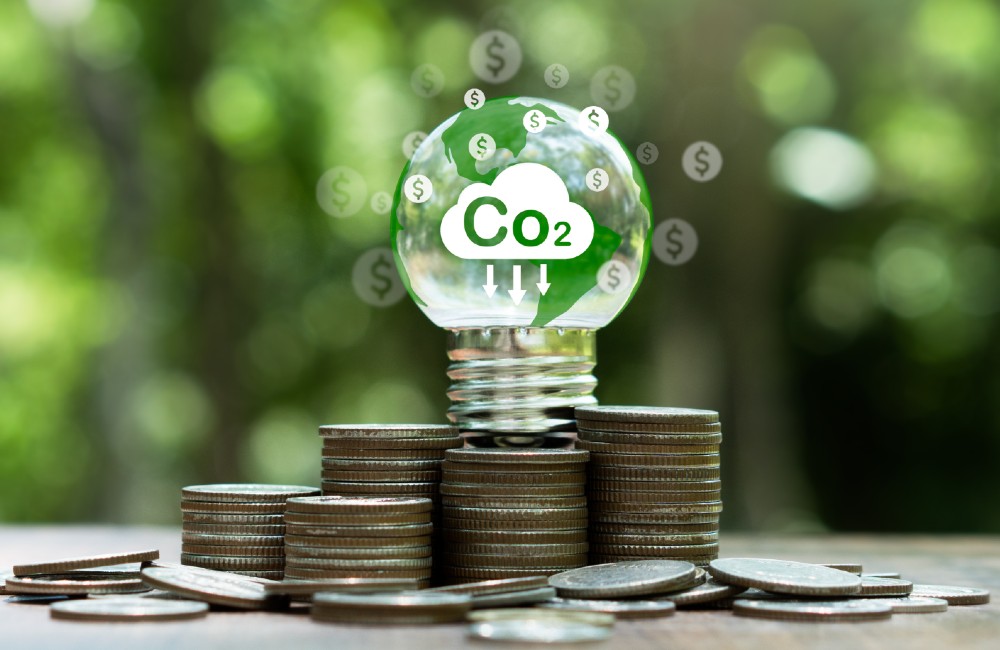 Glühbirne mit CO₂-Symbol auf gestapelten Münzen symbolisiert Einsparpotenzial durch CO₂-Reduktion und energieeffizientes Wirtschaften.