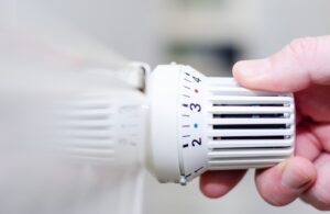 Hand dreht an einem weißen Heizkörper-Thermostat, eingestellt auf Stufe 3.